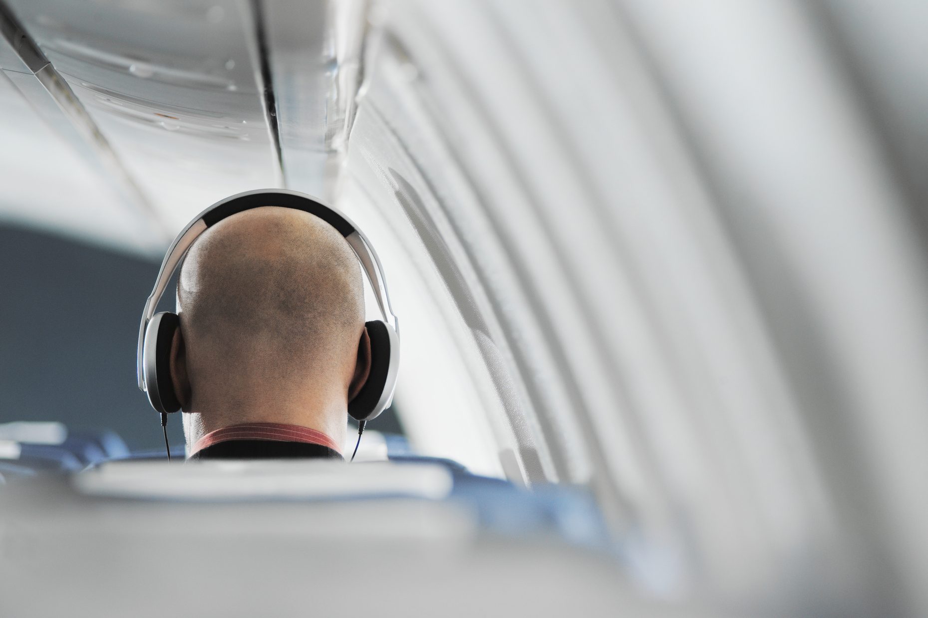 Businessman sitting on aeroplane seat, wearing headphones, rear view
