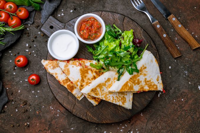 Quesadilla with chicken and sauces on dark board , on dark rustic concrete background