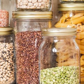 Shelf in the kitchen with various cereals and seeds - peas split, sunflower and pumpkin seeds, beans, rice, pasta, oatmeal, couscous, lentils, bulgur in glass jars