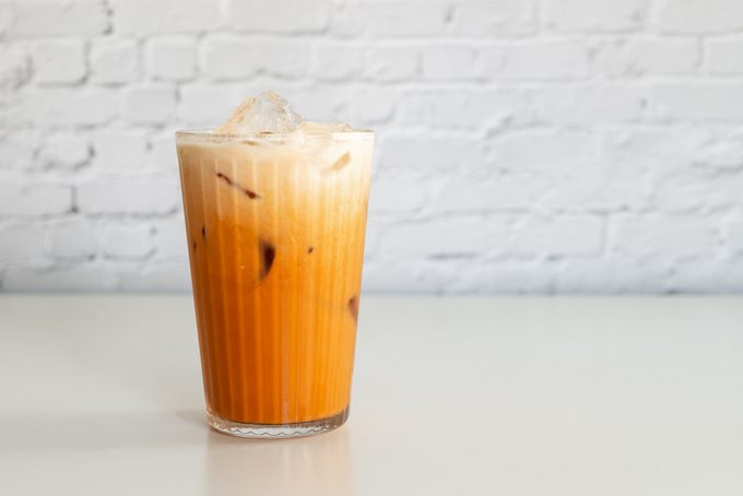 a glass of thai tea with milk on the white table.