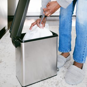 Close-up of unrecognizable black woman removing kitchen trash bag from can