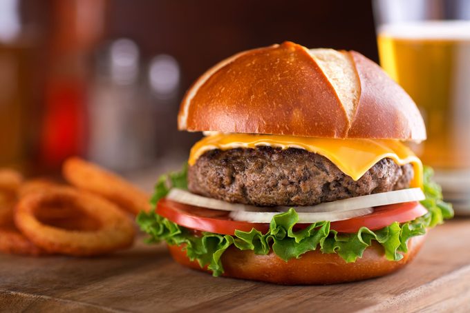 A delicious gourmet cheeseburger on a pretzel bun with lettuce, onion, and tomato.