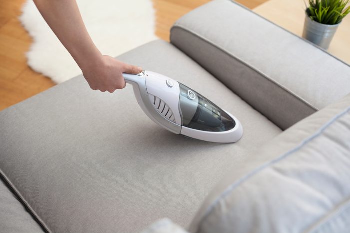 Woman with handheld vacuum cleaning on sofa