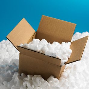 open cardboard shipping box with packing peanuts in a pile of packing peanuts against a blue background