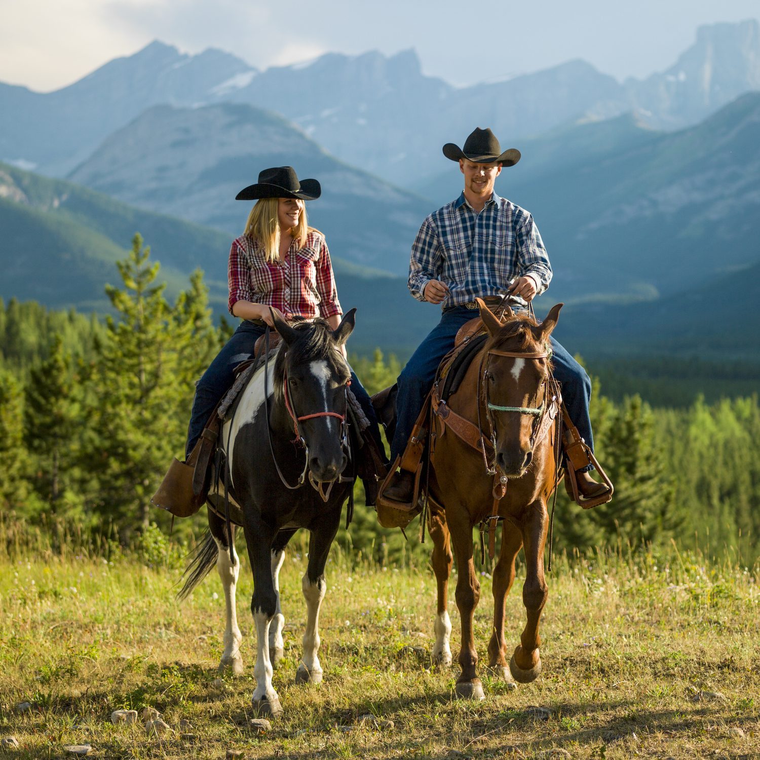 Cowboy and cowgirl ride horse thru mountain meadow