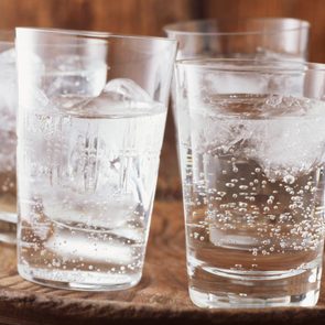 Sparkling water in drinking glass with ice on vintage wooden plate