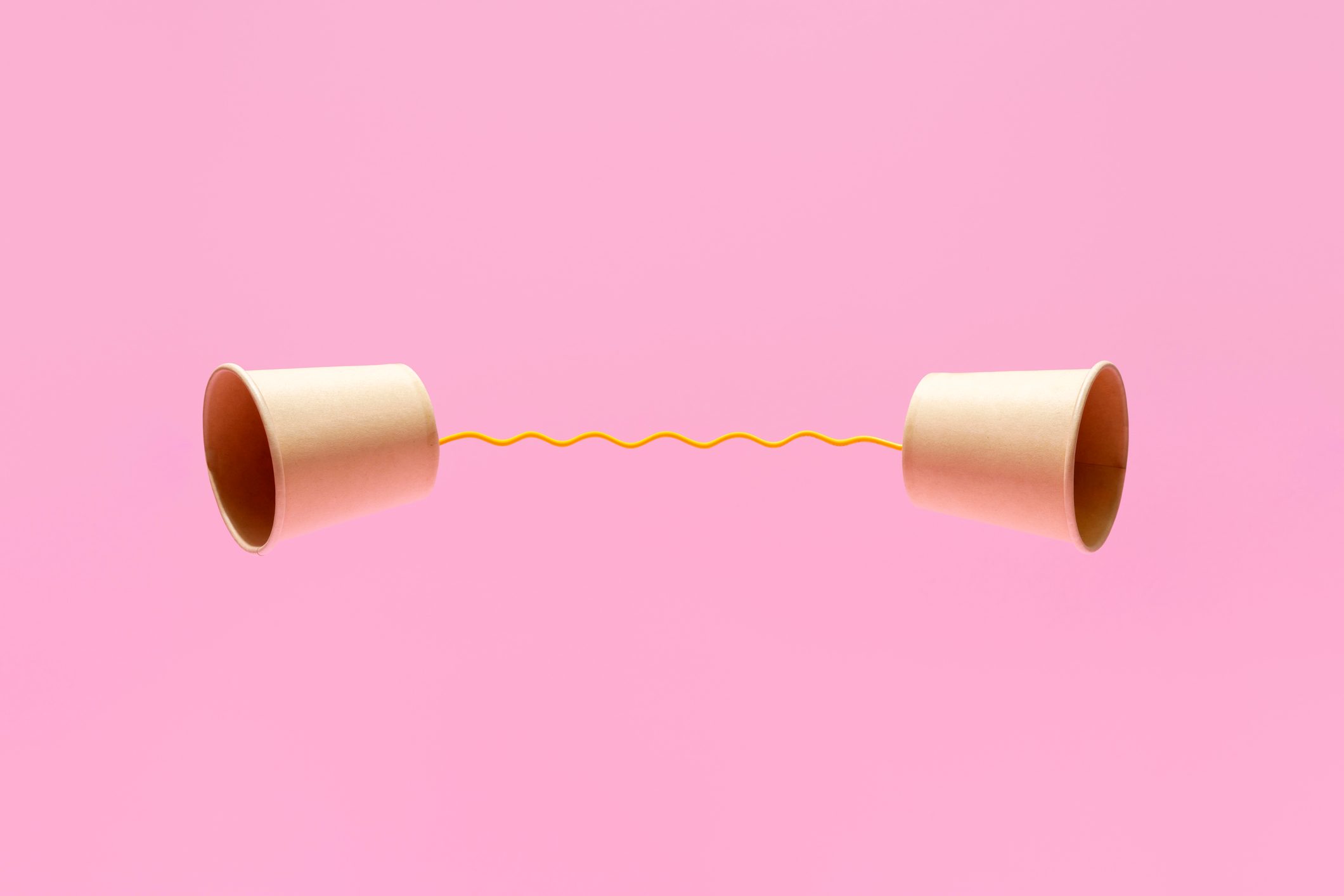 Two Paper Cups United With A Yellow String On A Pink Background