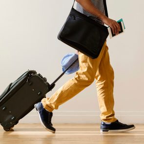 crop of lower half of businessman rolling luggage