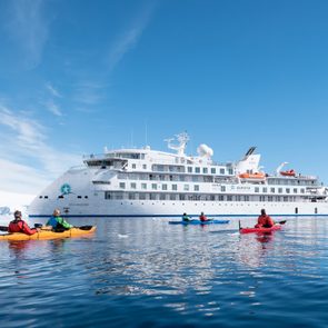 cruise ship with kayakers in front, snowy landscape in the background