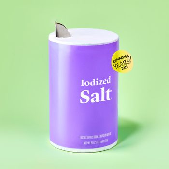 container of salt against green background. the container has an expiration sticker on it.
