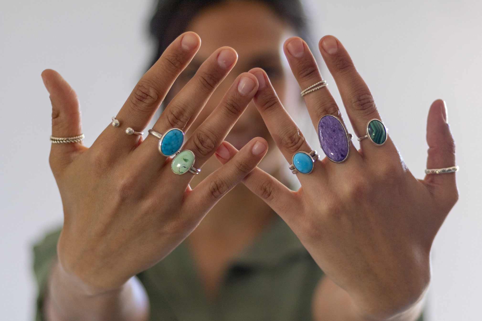 Woman showing hands with all fingers full of rings with colored stones.