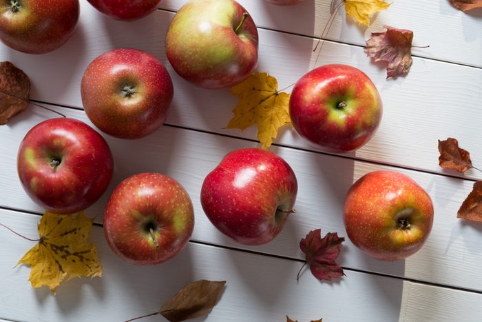 red apples on a white wood background with some autumn leaves