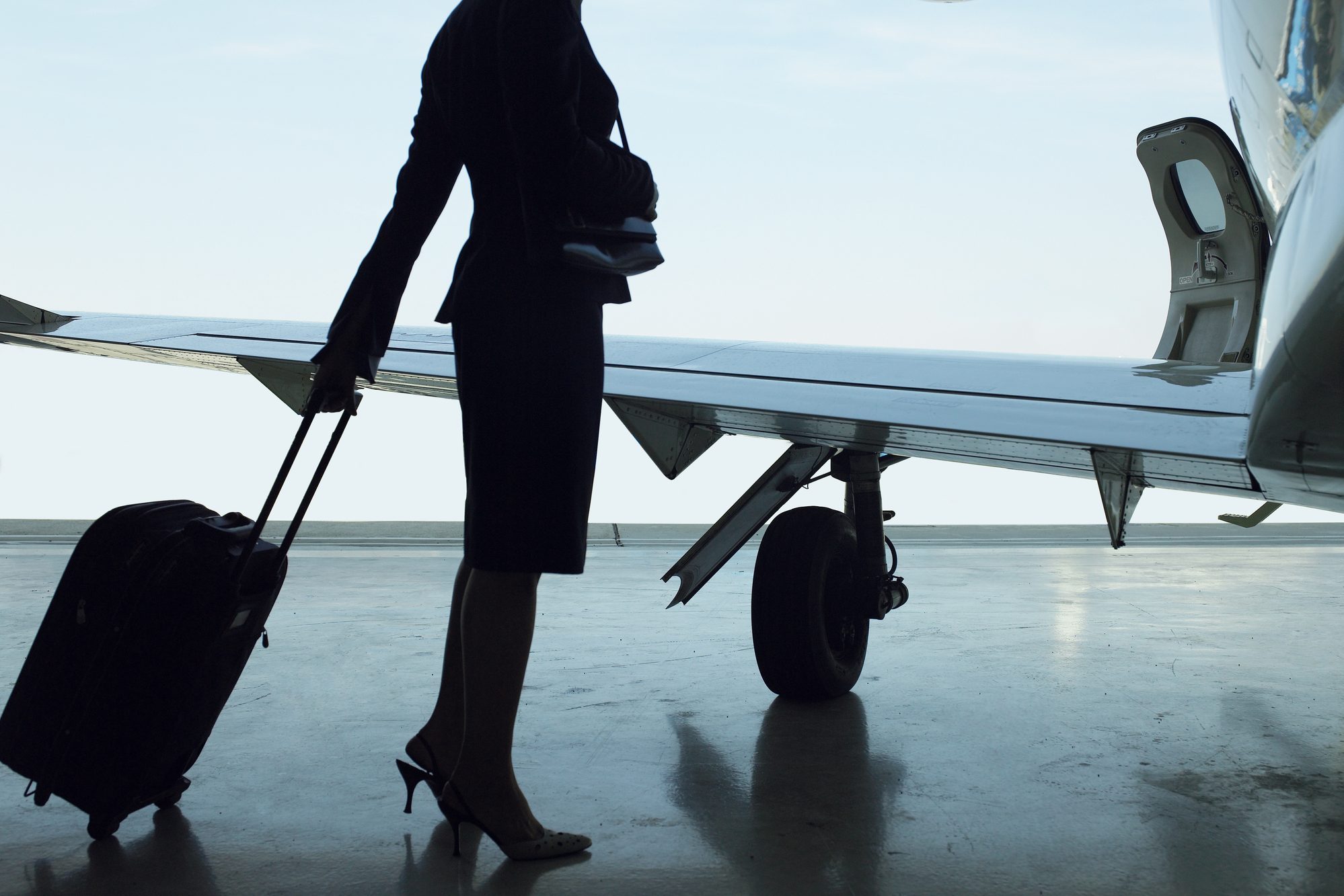 Flight attendant standing with suitcase near airplane, side view