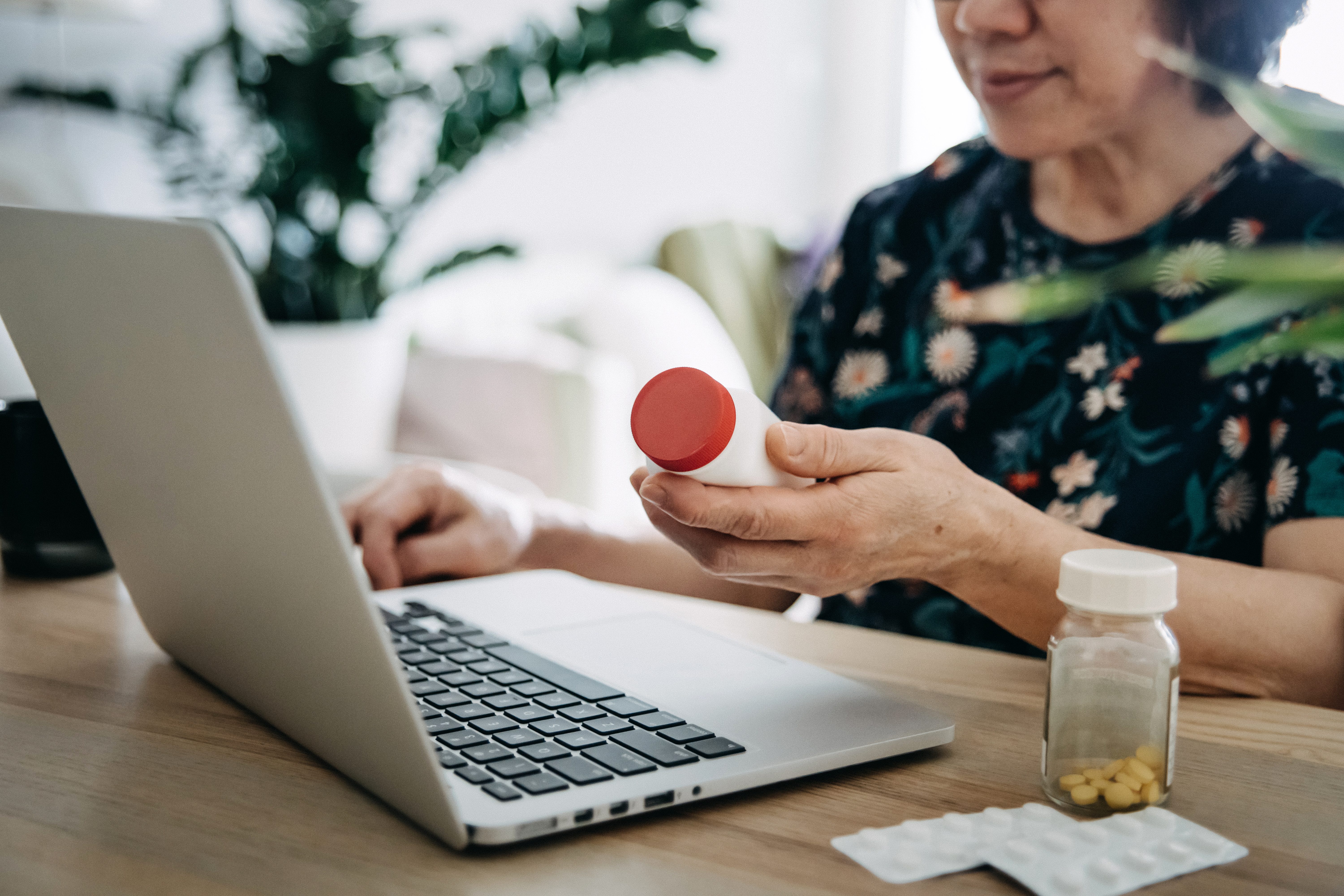 Senior Asian Woman Video Conferencing With Laptop To Connect With Her Family Doctor, Consulting About Medicine During Self Isolation At Home In Covid 19 Health Crisis