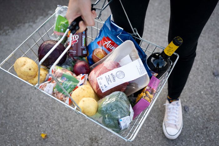 hands holding a grocery basket filled with food