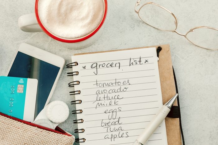 top view of grocery list, glasses, a purse with a credit card and phone and a mug of coffee