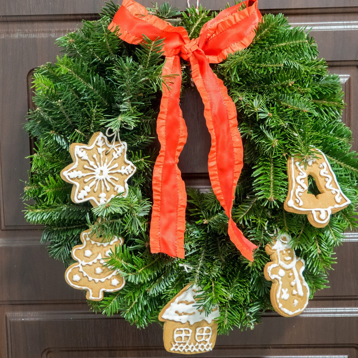 Christmas wreath decorated with handmade cookies and red ribbon hanging on the brown door.