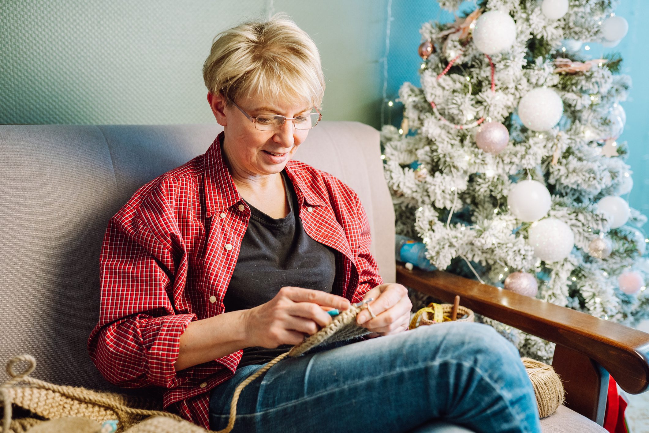 Creative mature woman knitting handmade presents at home on Christmas or new year holidays