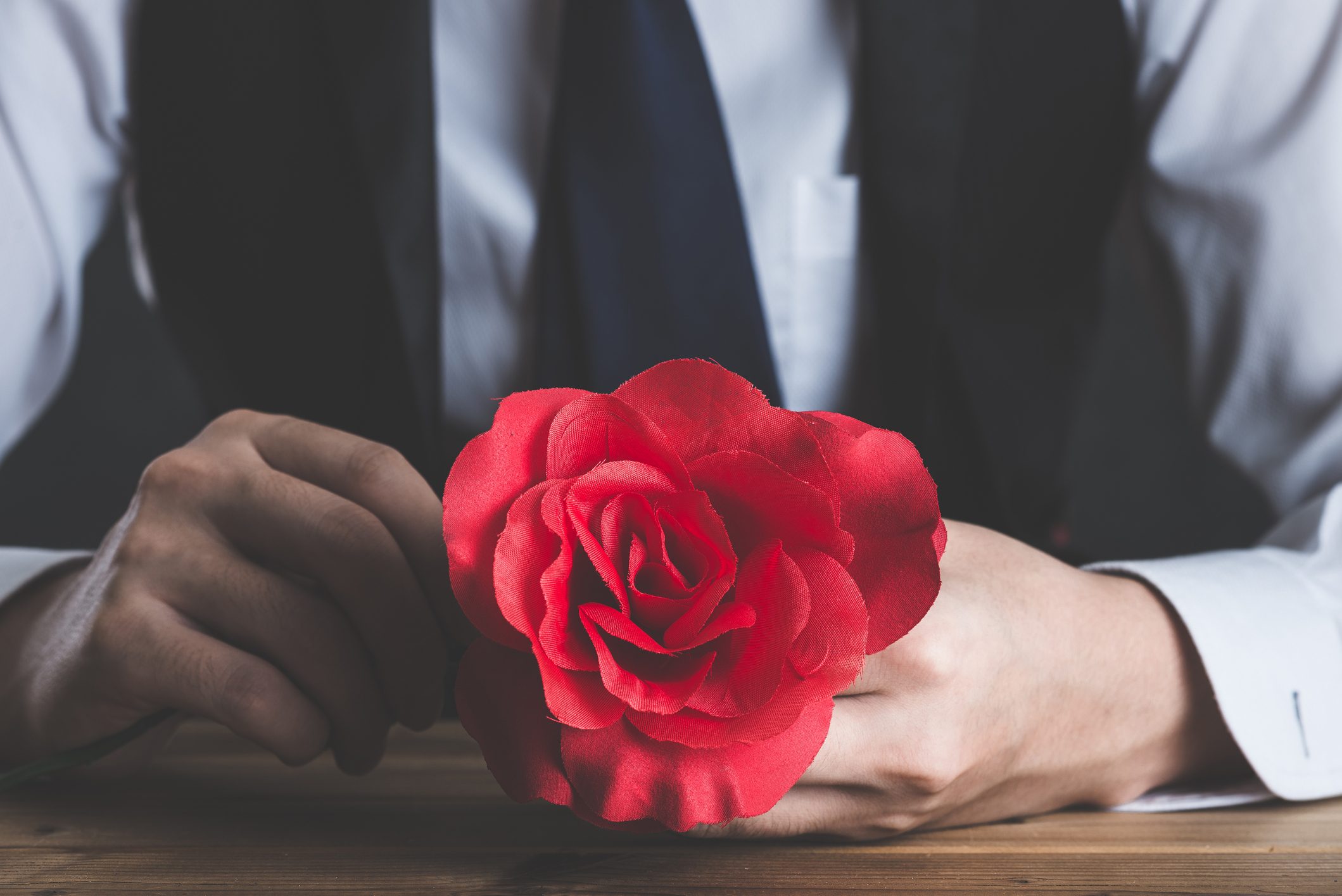 anonymous male figure in nice clothes holding a fake red rose flower