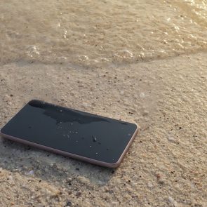 Mobile smart phone on the sandy beach with soft waves of sea background