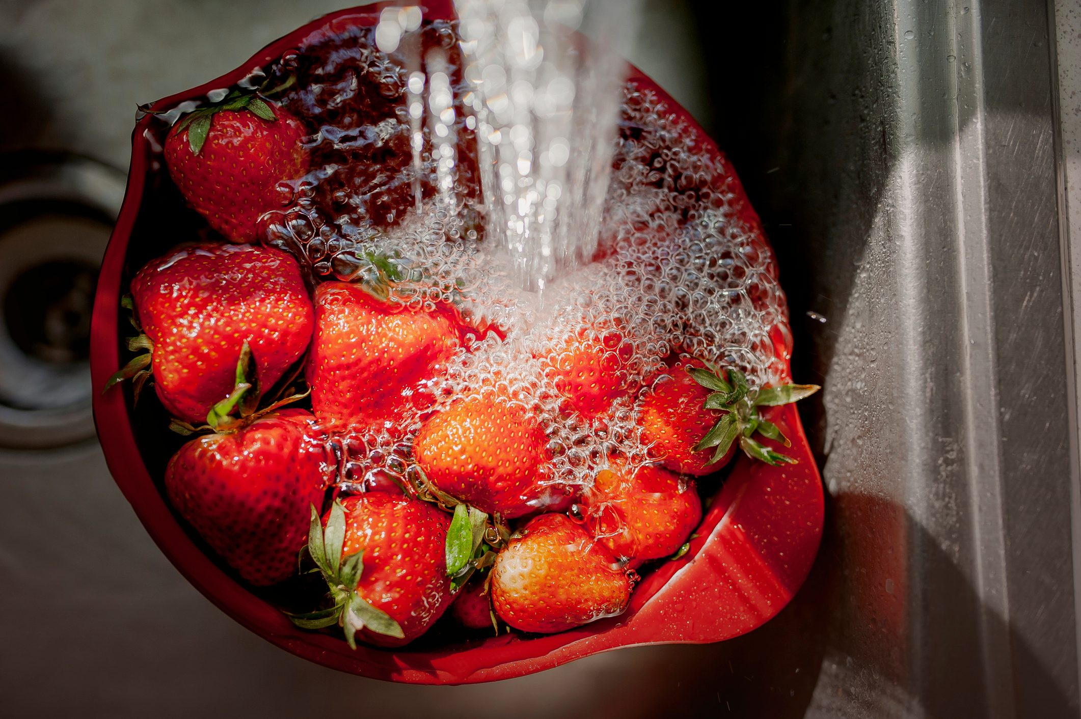 Bowl of Strawberries Under Running Water in a Kitchen Sink