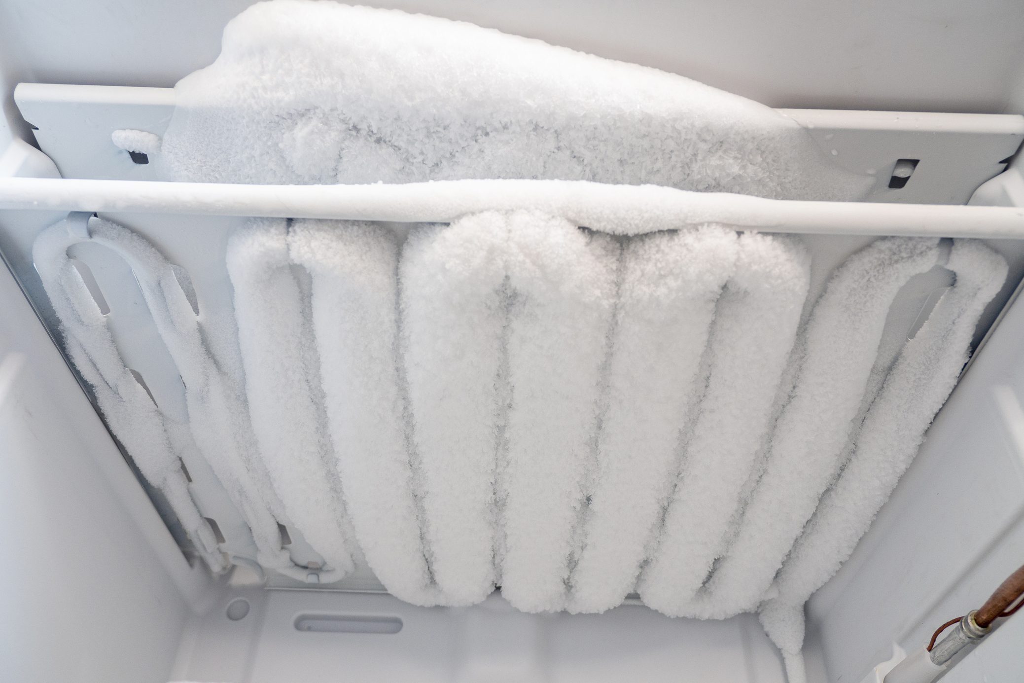 Close-up of opened deep freezer with ice and snow. Freezer before defrost. Empty shelves of fridge.