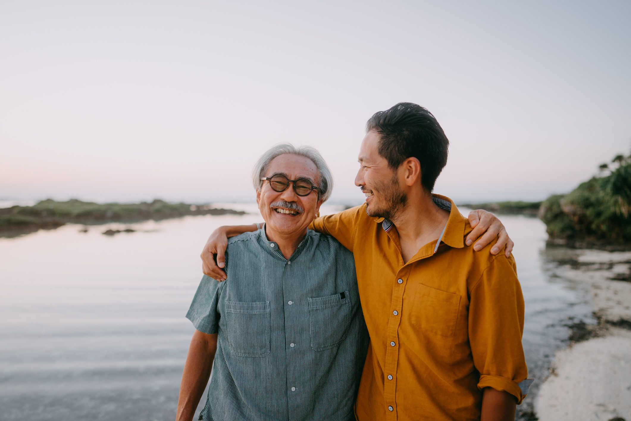 Senior father and adult son having a good time on beach at sunset