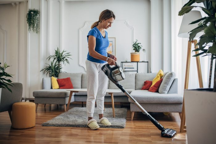 Woman vacuuming the living room with cordless vacuum cleaner