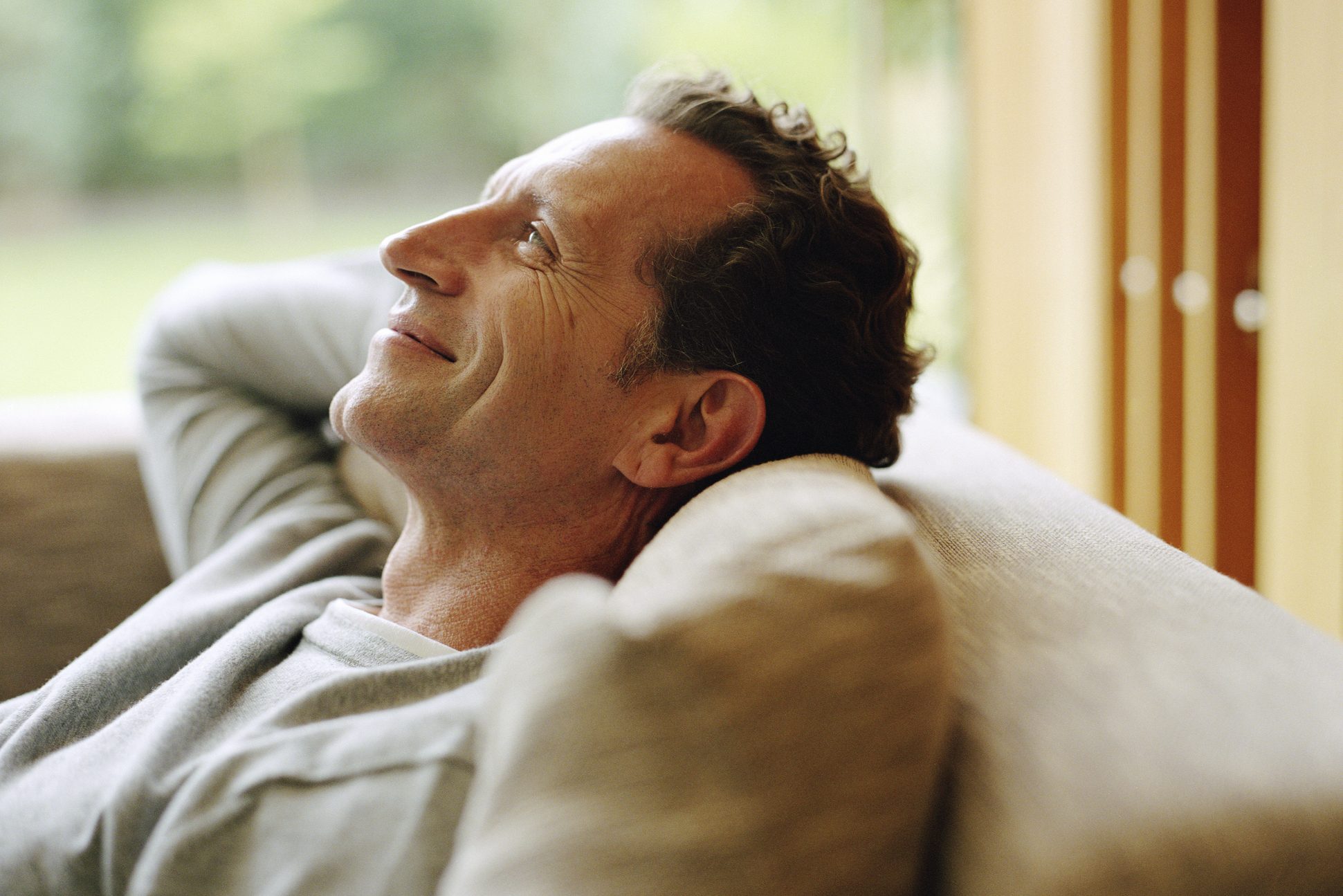 Mature man relaxing on sofa, hands behind head, smiling, profile