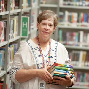 portrait of Martha Hickson standing in a library holding a stack of books