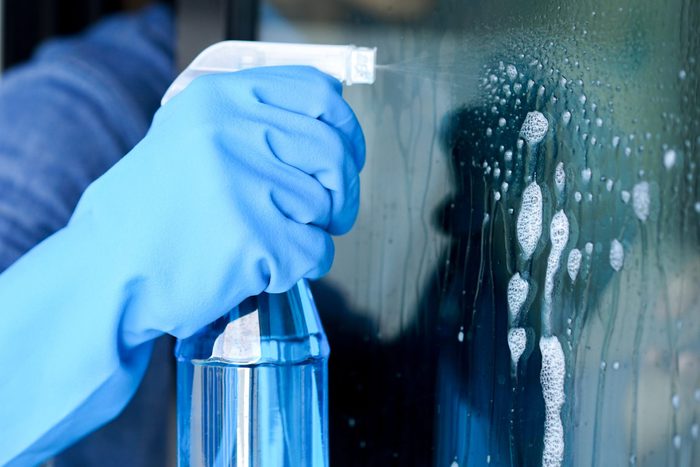 close up male housekeeper hand using spray bottle for cleaning dust on mirror door concept