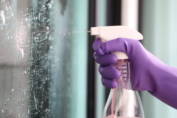 Close-Up Of Hand Spraying Liquid On glass