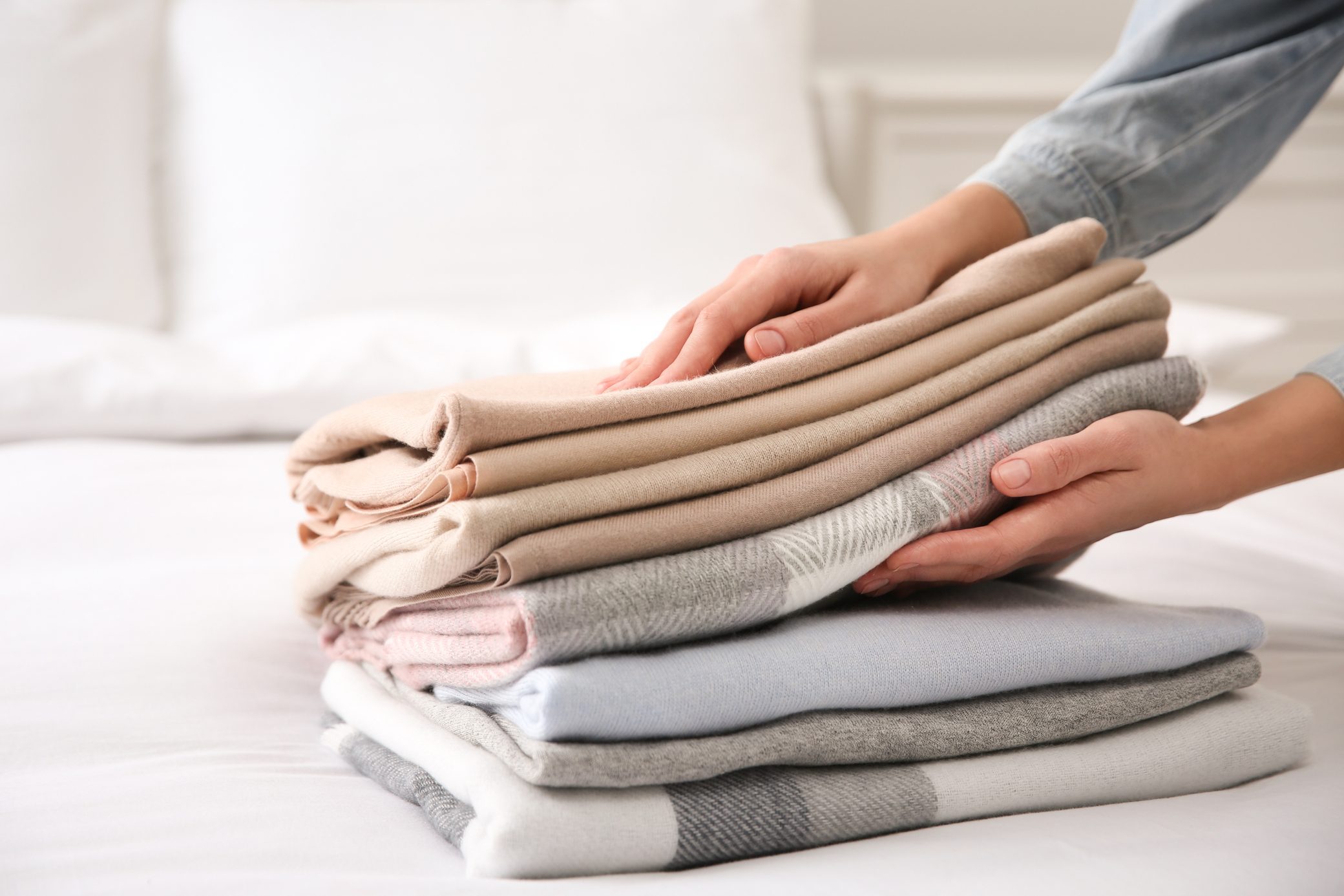 Woman with folded cashmere clothes on bed, closeup