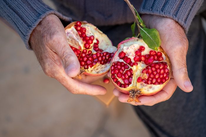 Ripe organic broken pomegranate, cut in half in senior hands .Selective focus,top view