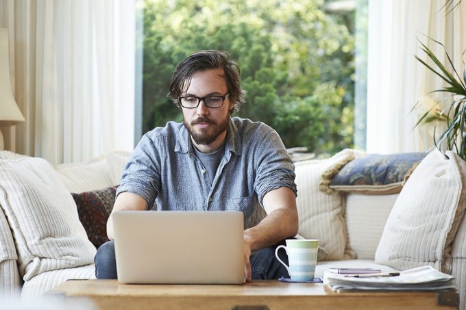 Man sitting on sofa and using laptop at home.