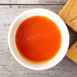 overhead view of Sriracha chilli sauce in a white bowl near a cutting board with a few chili peppers on it. wood background