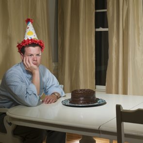 Mid adult man in party hat, sitting at table in front of birthday cake