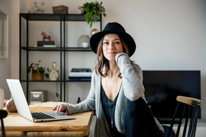 mature woman with hat, sitting at home, using laptop