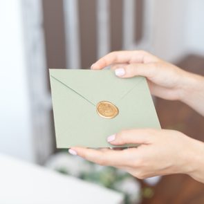 Close-up photo of female hands holding invitation envelope with a wax seal, a gift certificate, a postcard, wedding invitation card.