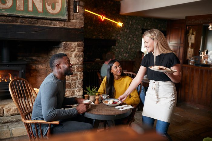 Waitress Working In Traditional English Pub Serving Breakfast To Guests