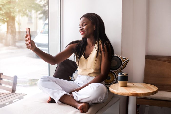 Attractive african girl makes selfie at the windowsill at cafe.