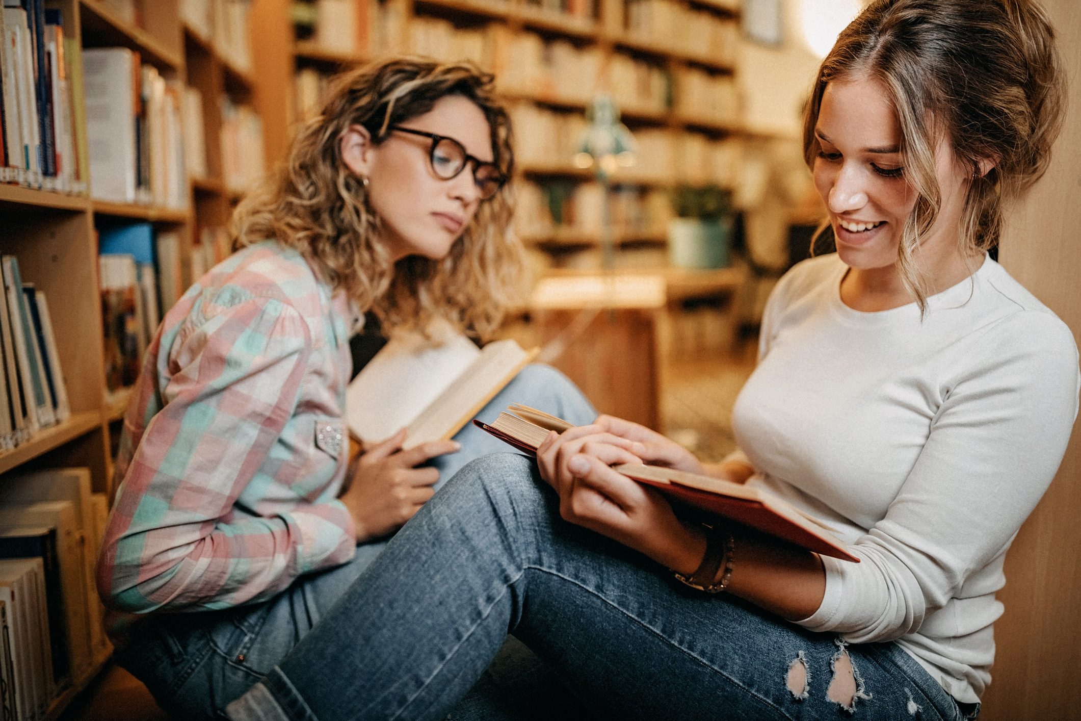 two women reading poetry to each other on a library floor