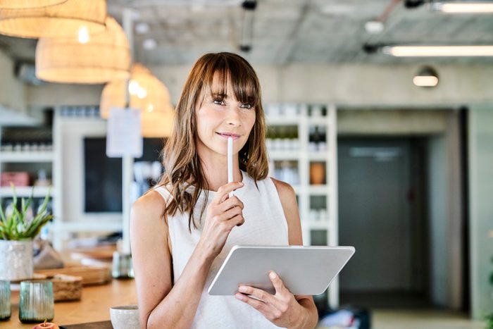 Thoughtful woman holding digitized pen and digital tablet while standing art home