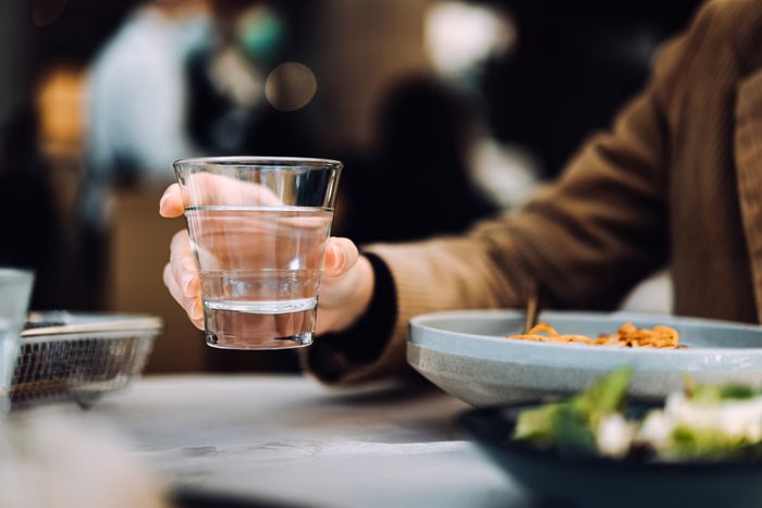 Close up of young Asian woman drinking a glass of water while having meal in a restaurant. Healthy lifestyle and stay hydrated