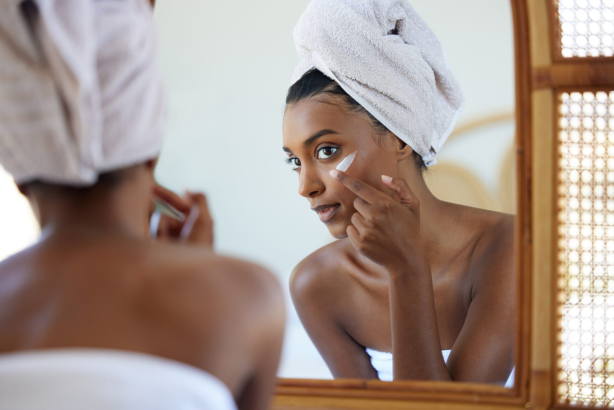 Shot of a beautiful young woman applying moisturiser while looking into the bathroom mirror