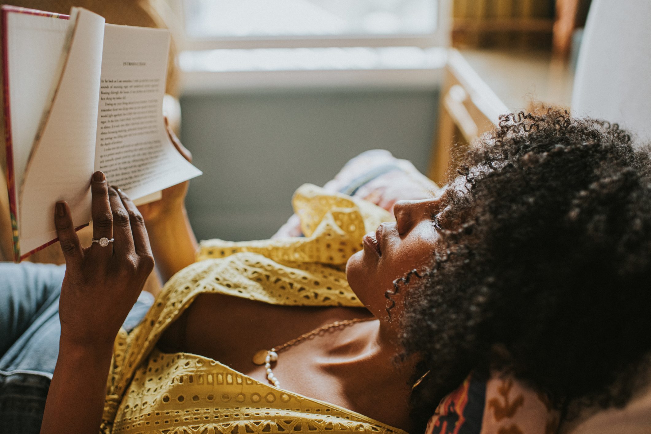 A content woman reclines on a comfortable bed and gets lost in a good book