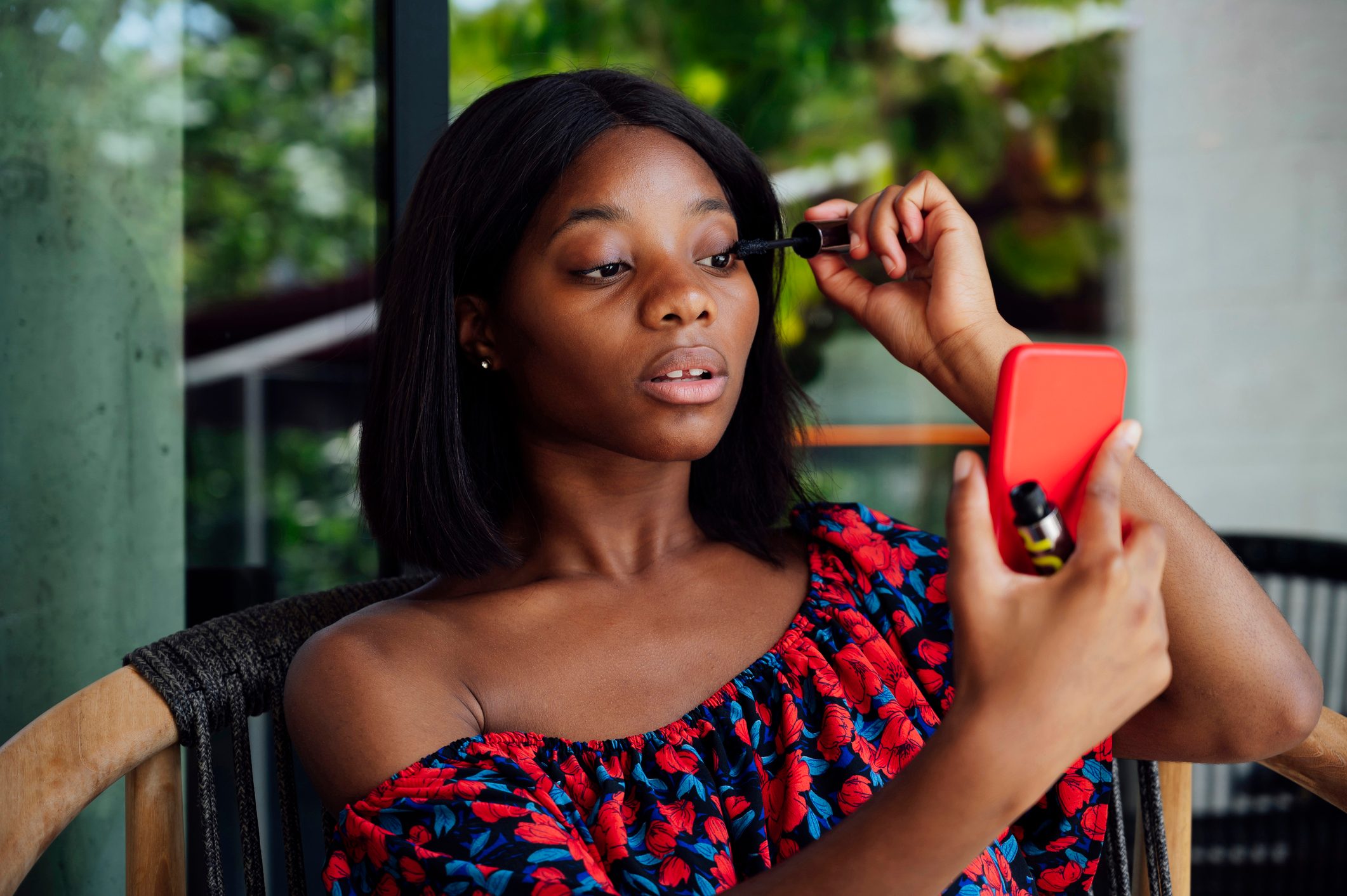 Young woman applying mascara looking at smart phone