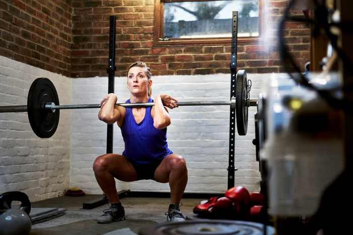 Woman exercising in home gym in converted garage performing a squat or clean