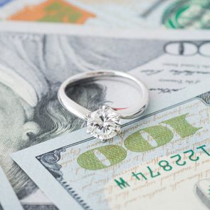 a diamond engagement ring sitting atop some scattered hundred dollar bills