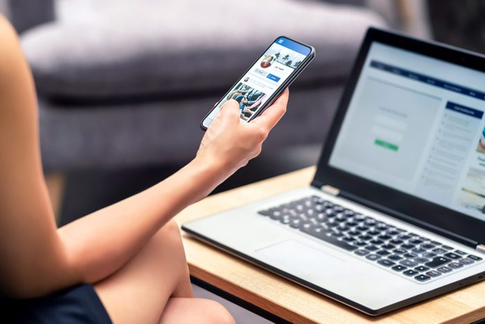 Social media profile page in smartphone screen at work. Woman looking at feed, status update or post with mobile phone. Inefficient lazy worker avoiding job.